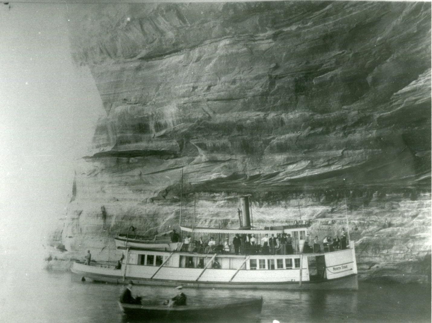 A steamer and rowboat in the Grand Portal of the Pictured Rocks in the early 1900s. Grand Portal collapsed in 1906. PC: the Alger County Historical Society.