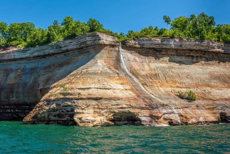 The convex outcropping of the Pictured Rocks Cruise tour highlight, Bridaveil Falls, with water streaking down the cliff facade