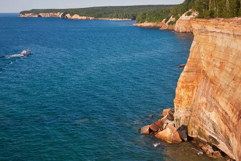 A Pictured Rocks boat tour passes in the distance, as the cliffs of Gull Rookery is in the foreground