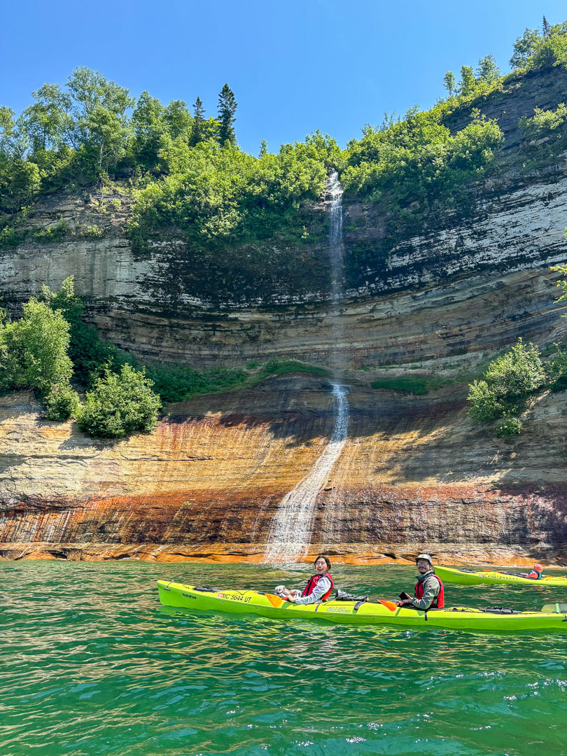 couple in a tandem kayak beside a cliffside waterfall at Pictured Rocks