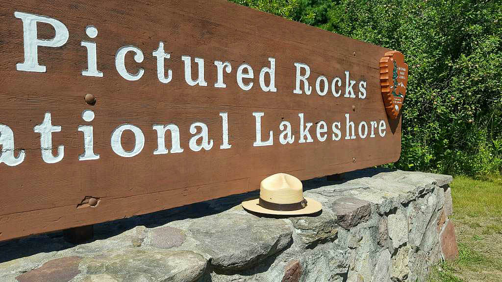 The wooden Pictured Rocks National Lakeshore park sign on a stone base with a ranger hat resting on it